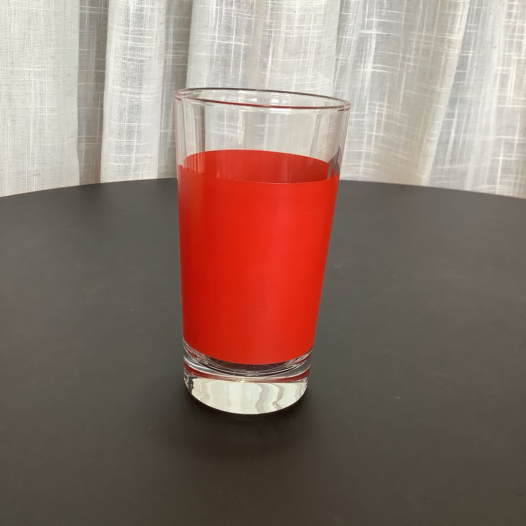 Clear glass filled with red stripe on a dark surface with a light curtain background