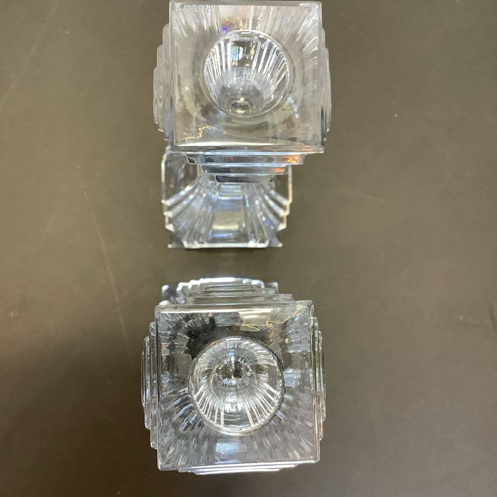 Two clear glass candle holders on a reflective surface