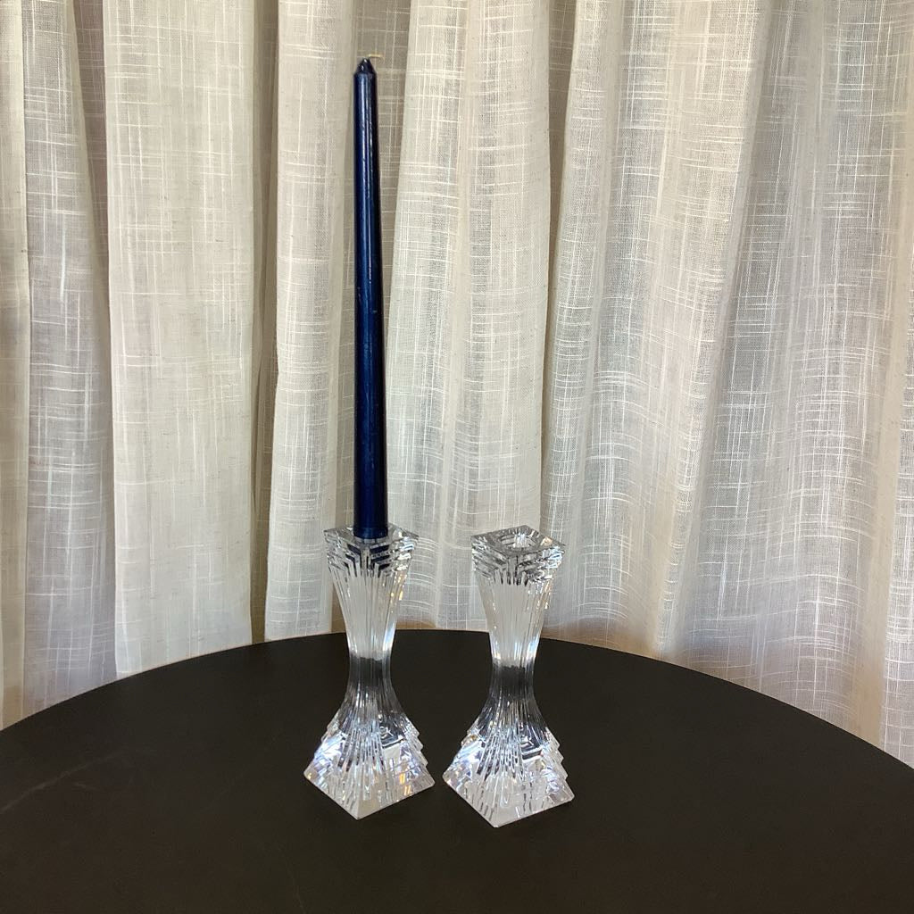 Two crystal candle holders with a blue candle on a black surface and beige curtain background