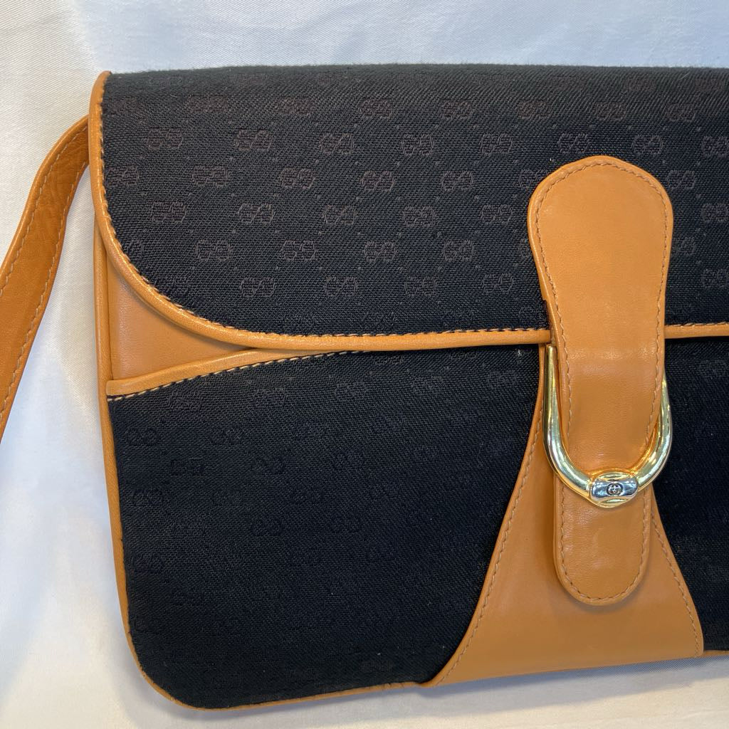 A Gucci shoulder bag featuring black GG Supreme canvas and tan leather trim, with a gold-tone metal D-ring closure on the front flap.