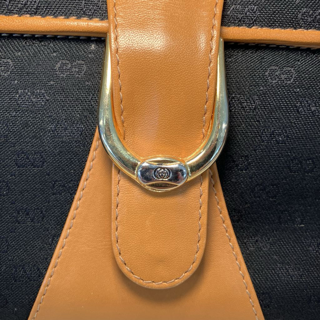 Close-up of a luxury handbag featuring a tan leather strap with a polished silver-tone metal D-ring closure, set against a black and gray repeating monogram canvas background.