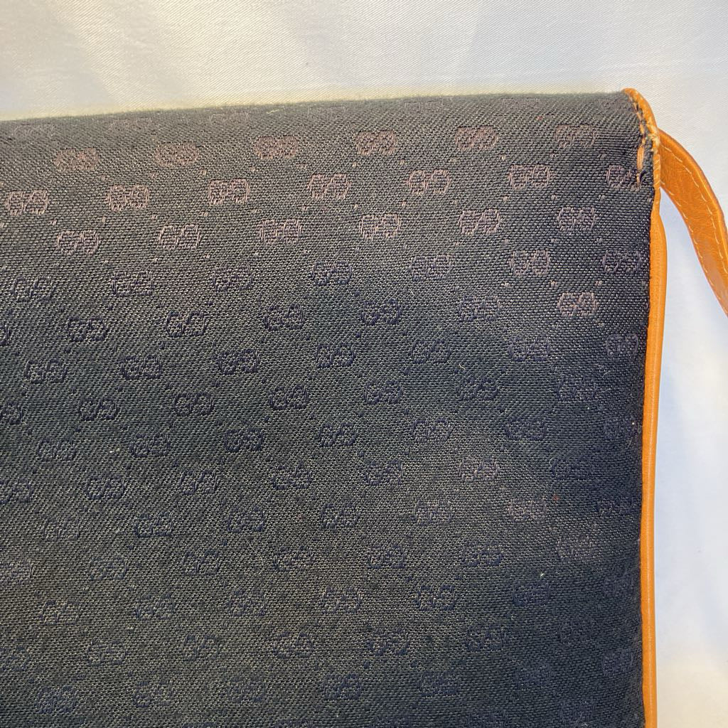 Close-up of a dark gray woven fabric with an allover repeating monogram pattern, showing a bright orange leather trim and strap on the right side.