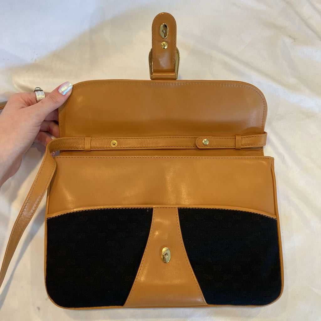 A tan leather and black faux-suede shoulder bag with gold-tone hardware, held open by a hand over a white fabric background.
