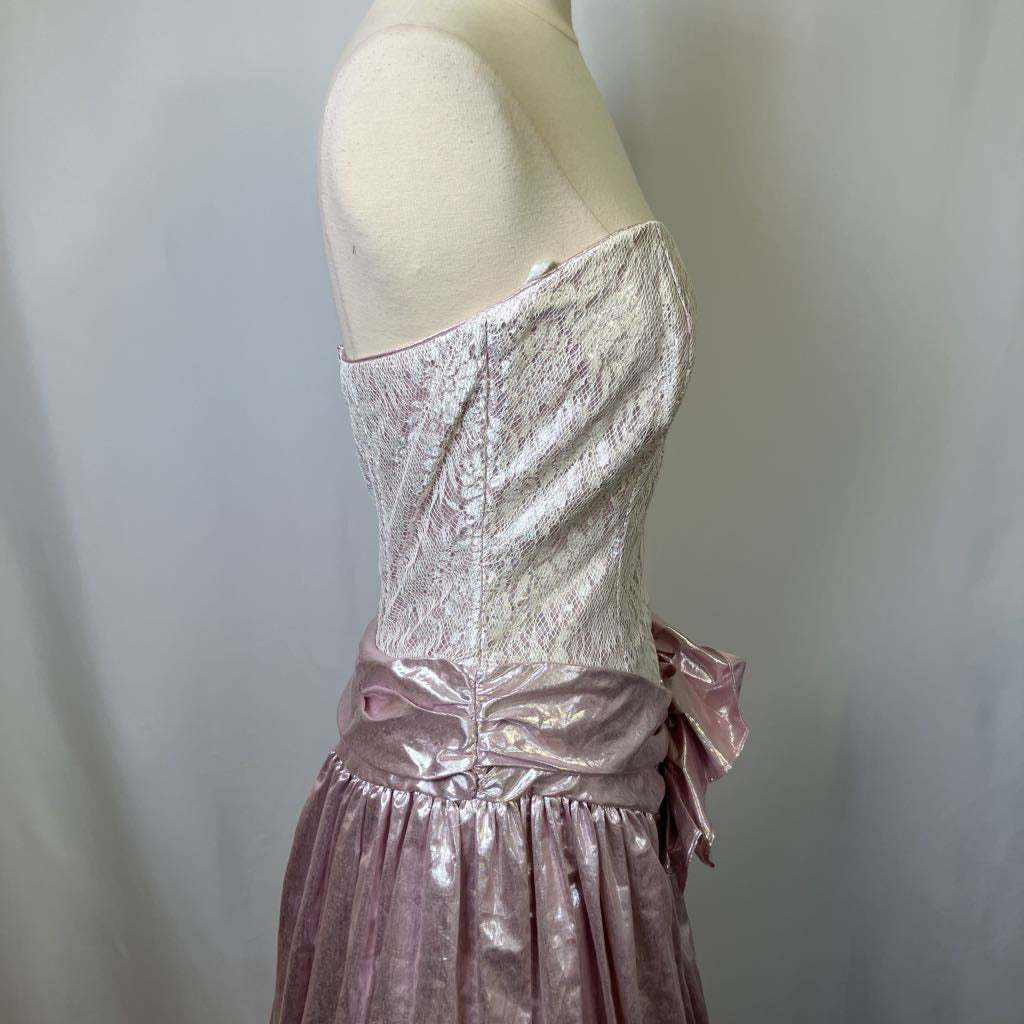 Mannequin wearing a pink lace dress with a bow detail on a plain background