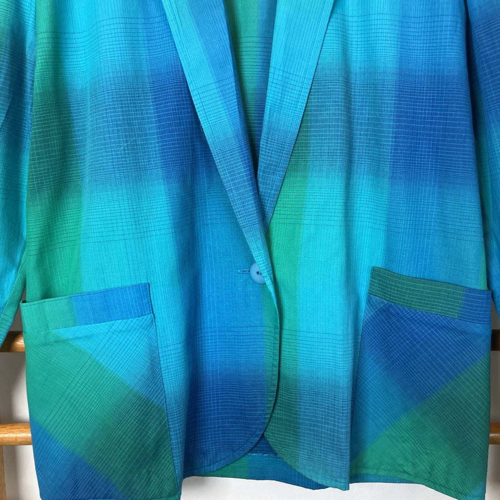 Blue and green gradient jacket on a wooden hanger against a white wall.