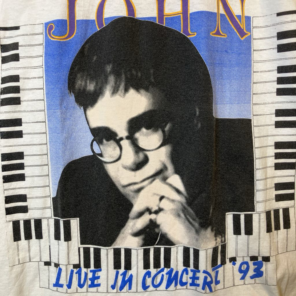 T-shirt with a graphic of a person with glasses and text 'JOHN LIVE IN CONCERT '93' on a background with piano keys.