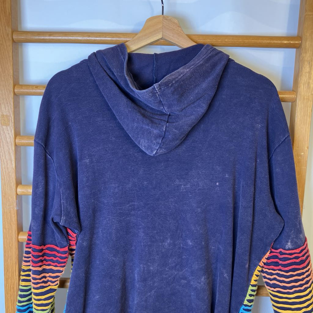 Blue hoodie with colorful sleeves on a wooden hanger against a wooden rack.