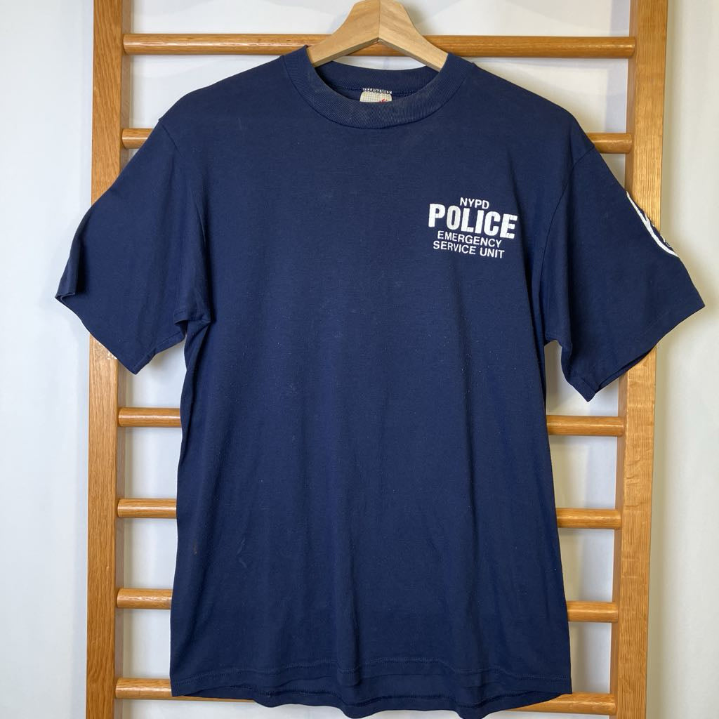 Navy blue t-shirt with 'POLICE EMERGENCY SERVICES UNIT' text on a wooden rack.