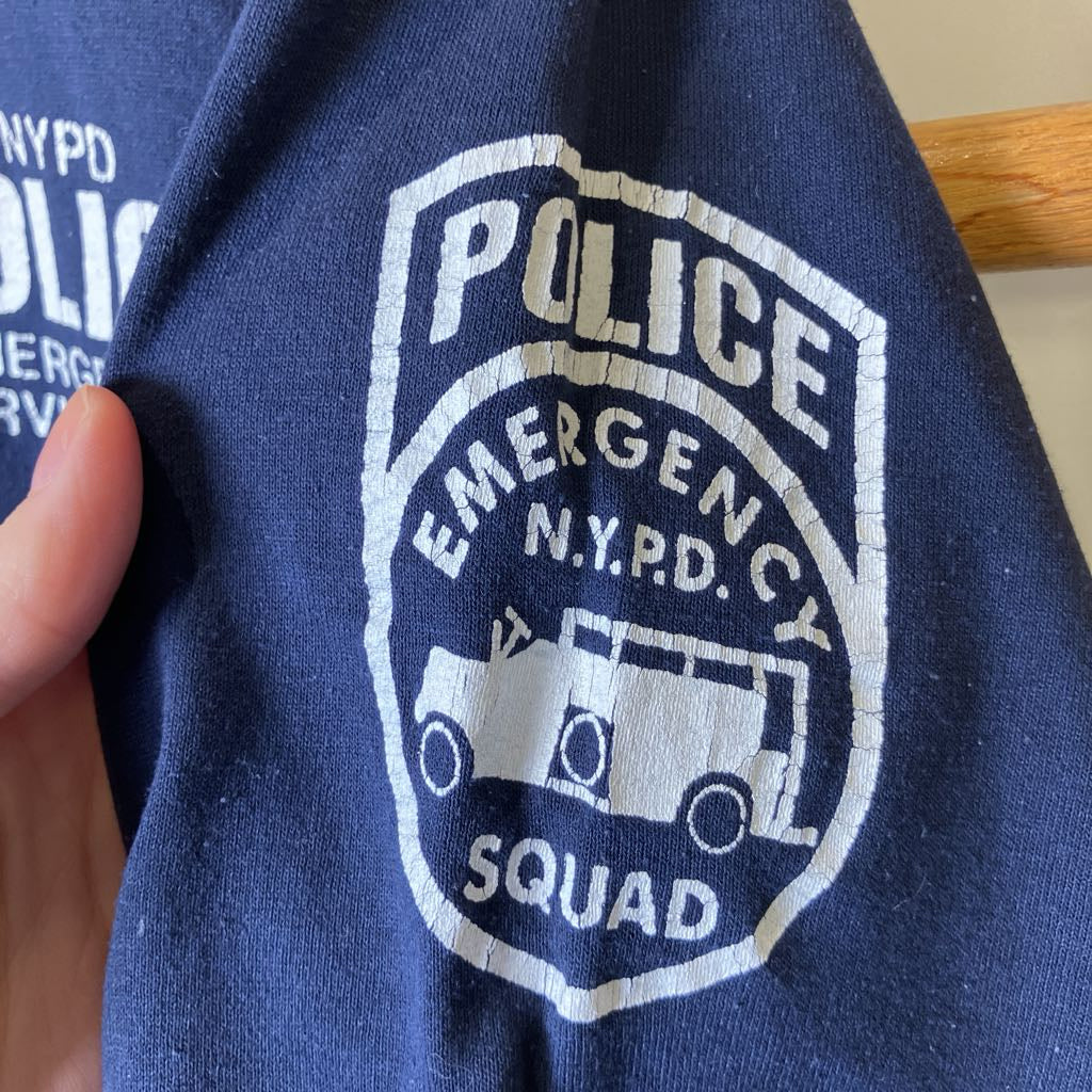Blue shirt with a white 'Police Emergency N.Y.P.D. Squad' logo on a wooden surface.