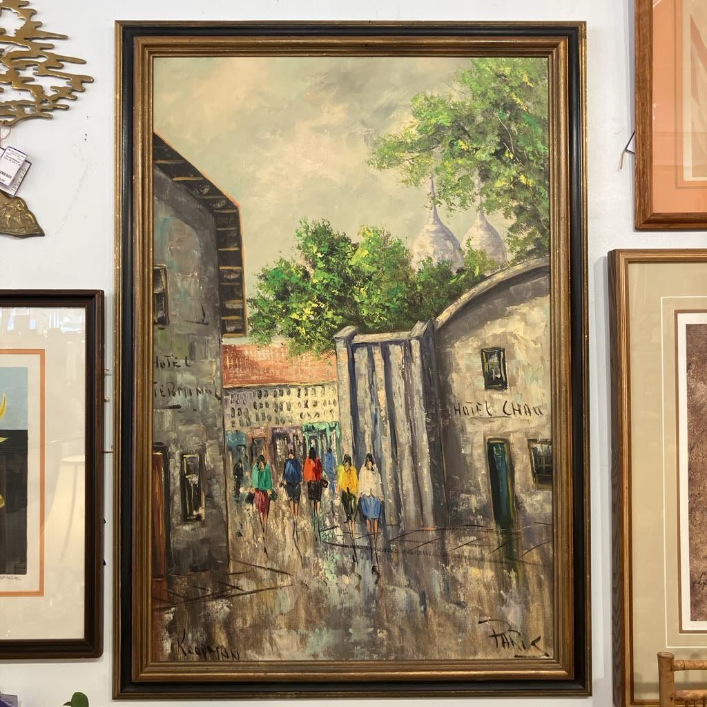 Framed painting of a city street scene with people walking, displayed on a wall with other framed artworks.