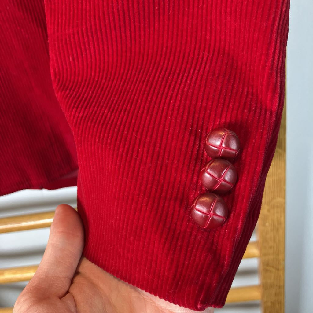 Close-up of a red textured fabric with three buttons held by a hand.
