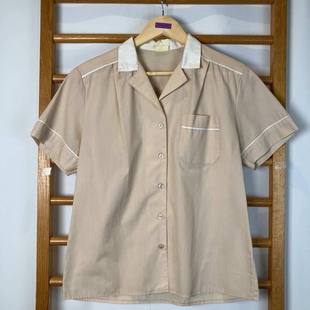 Beige shirt with white trim on a hanger against a wooden rack.