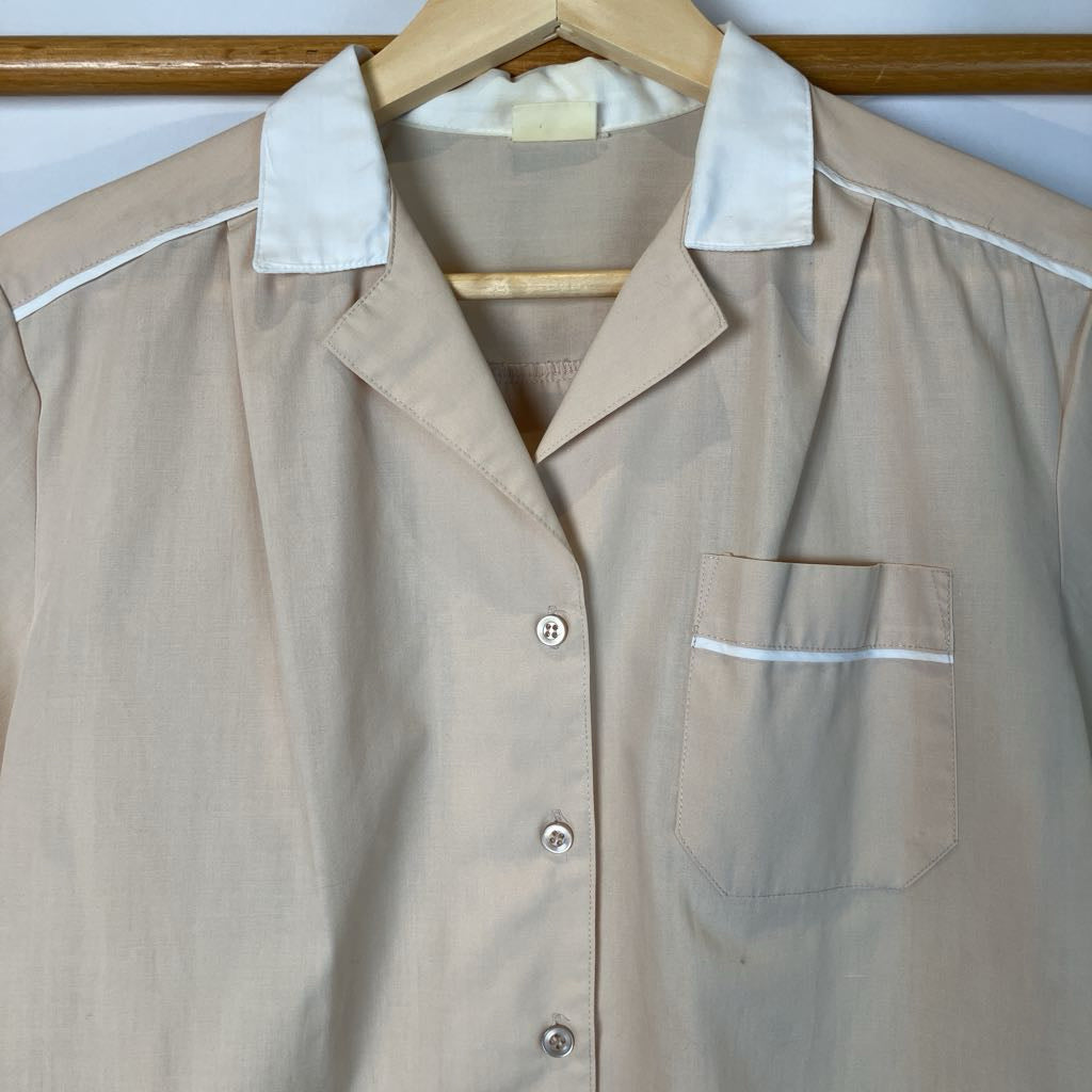 Beige shirt with white trim on a hanger against a white wall