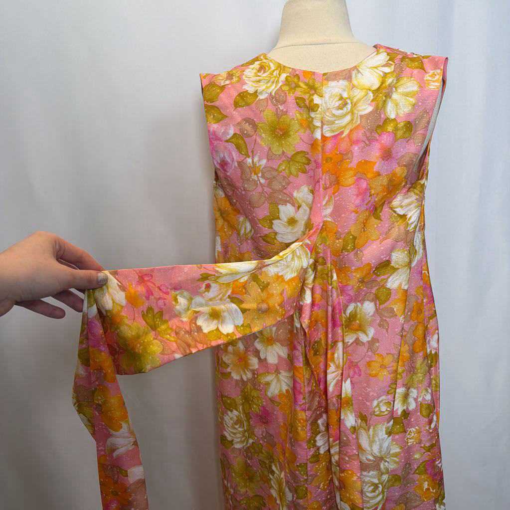 Floral dress on a mannequin with a hand adjusting the fabric against a plain background