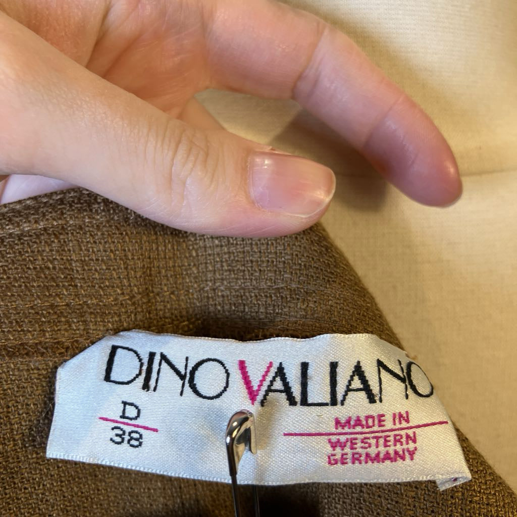 Close-up of a Dino Valiano label on a garment with a hand pointing to it.