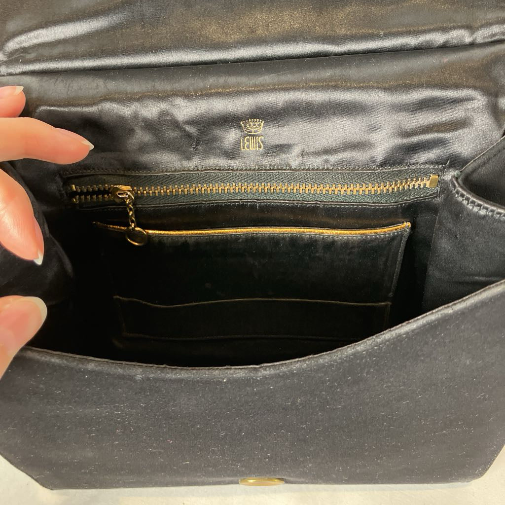 Black leather handbag with gold zipper and visible brand logo, held by a hand.