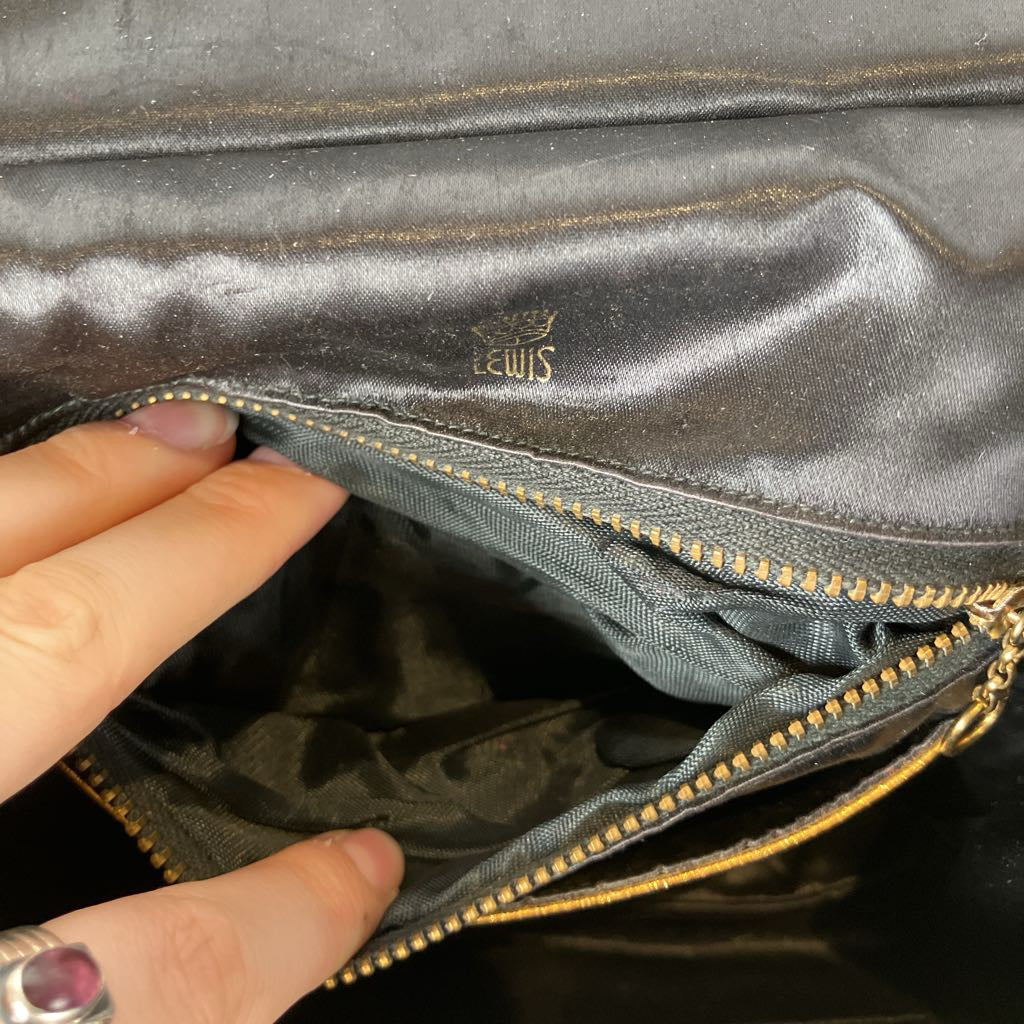 Black fabric with a hand holding open a pocket with a gold zipper.