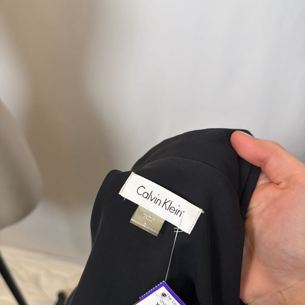 Black garment with a Calvin Klein label held by a hand against a neutral background