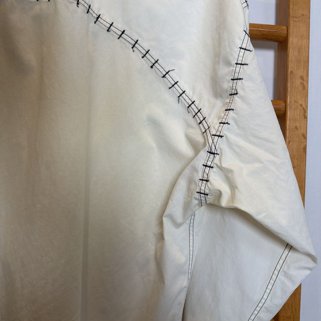 Close-up of a white garment with black stitching on a wooden surface.