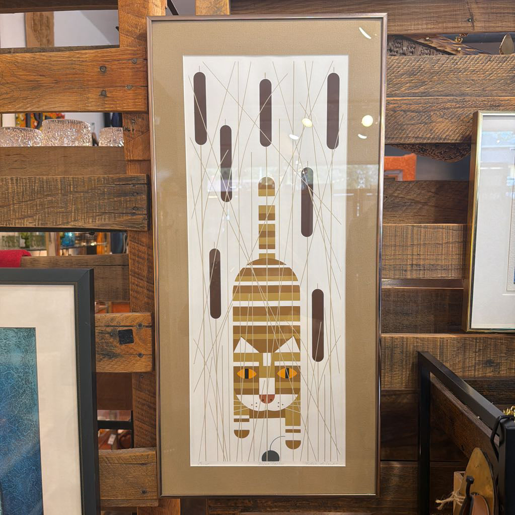 Framed abstract artwork of a cat on a wooden shelf with other framed items.