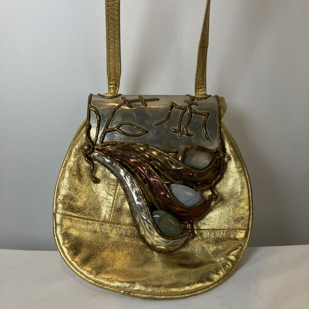 Gold handbag with decorative flap featuring a leaf design on a white background