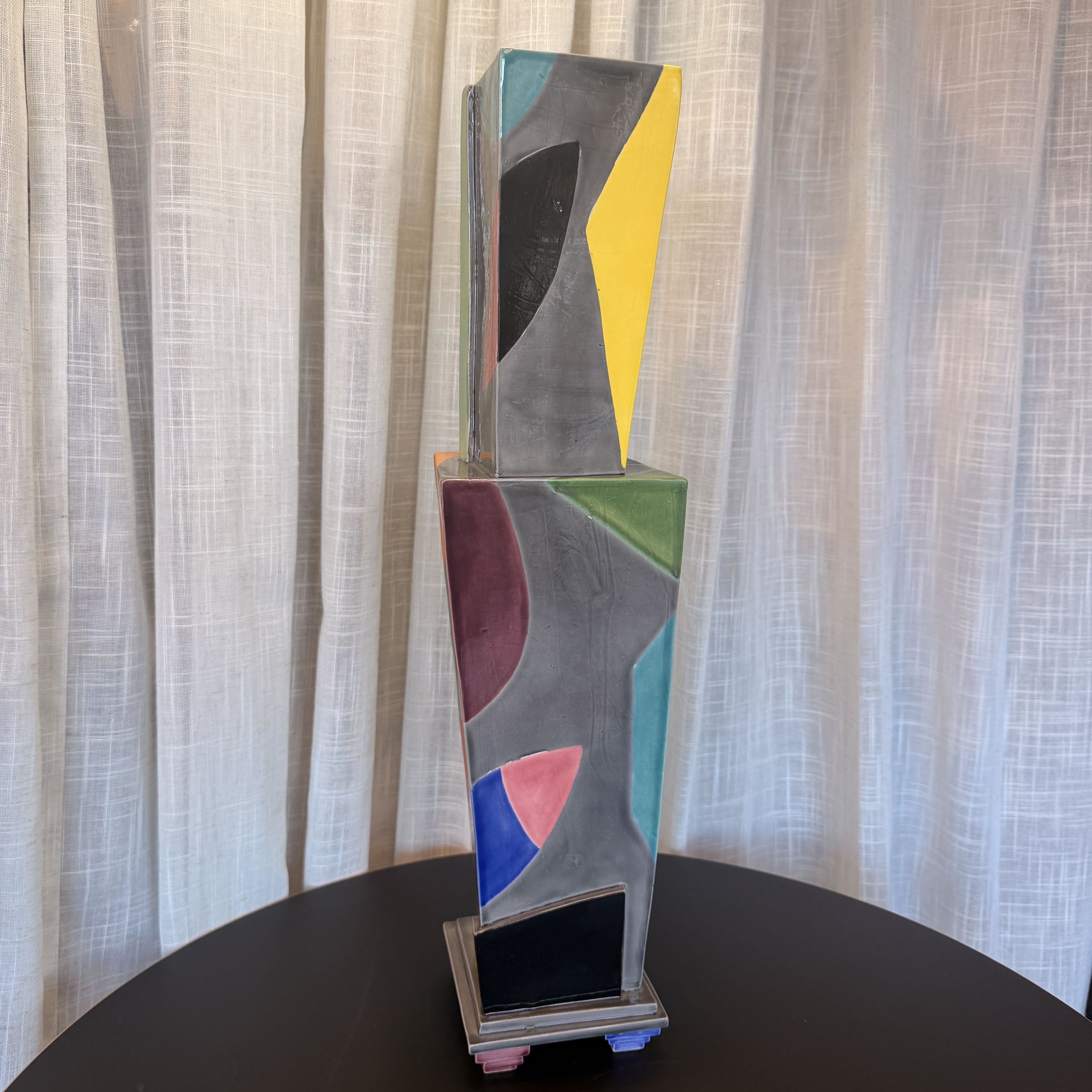 Abstract art sculpture on a black surface with a light gray curtain background