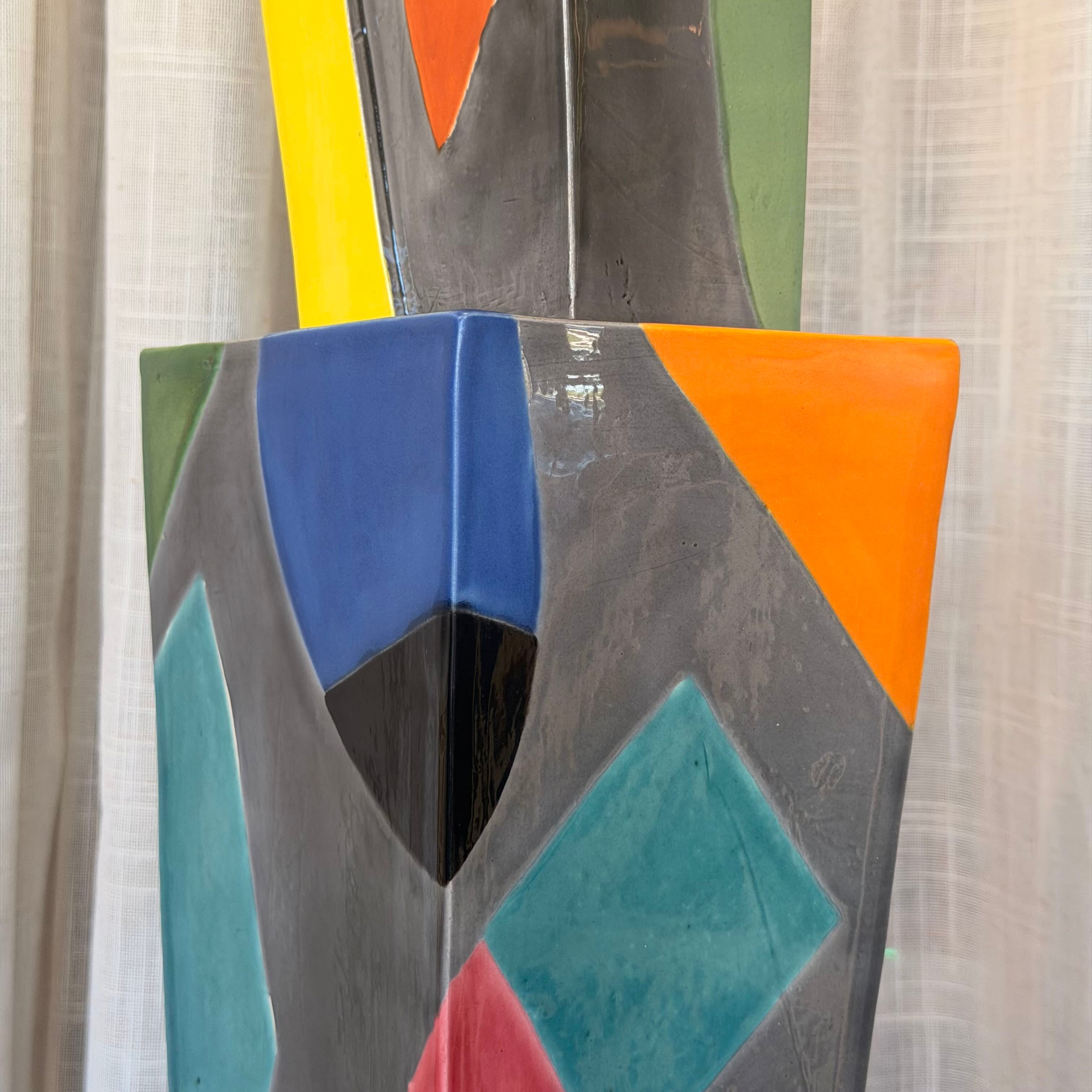 Abstract art piece with geometric shapes in various colors on a textured wall.