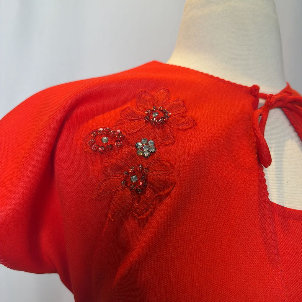 Red top with floral embellishments on a mannequin against a white background