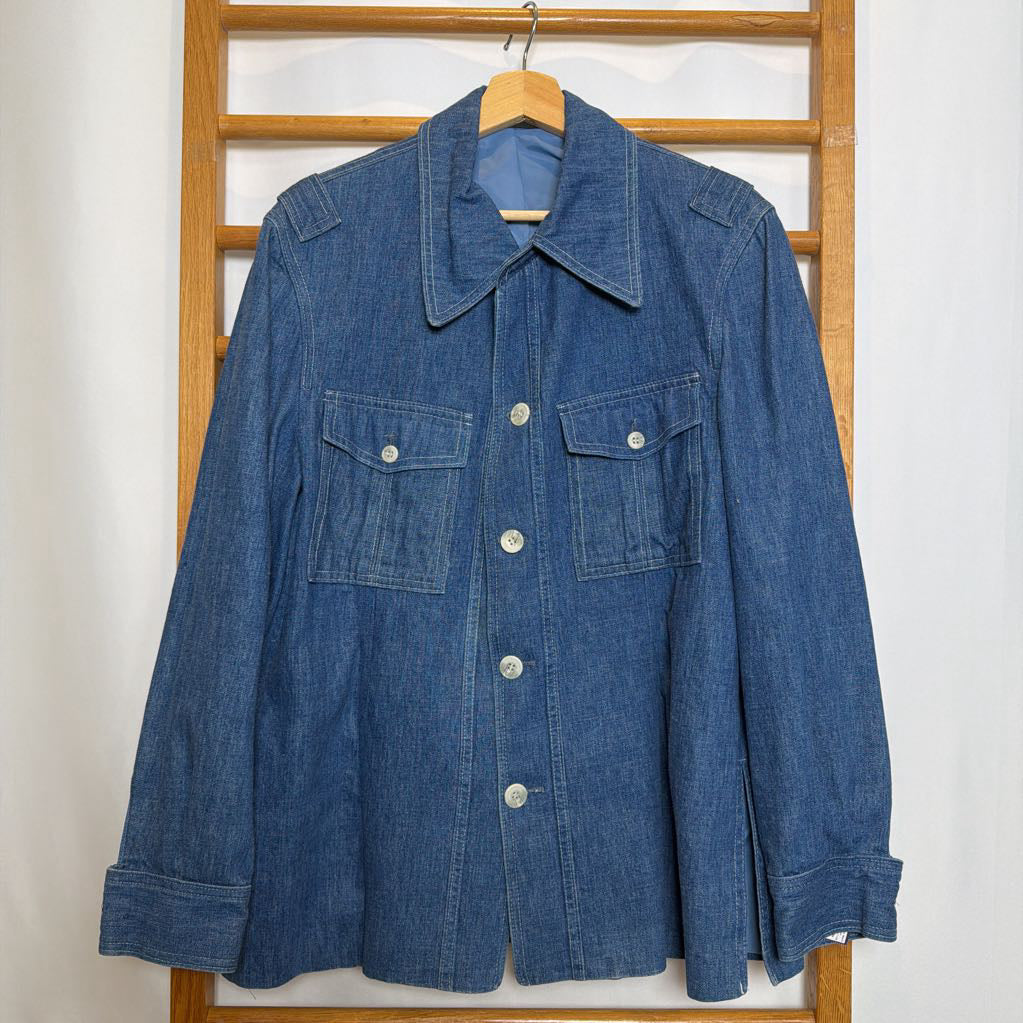 Blue denim jacket on a wooden hanger against a white wall