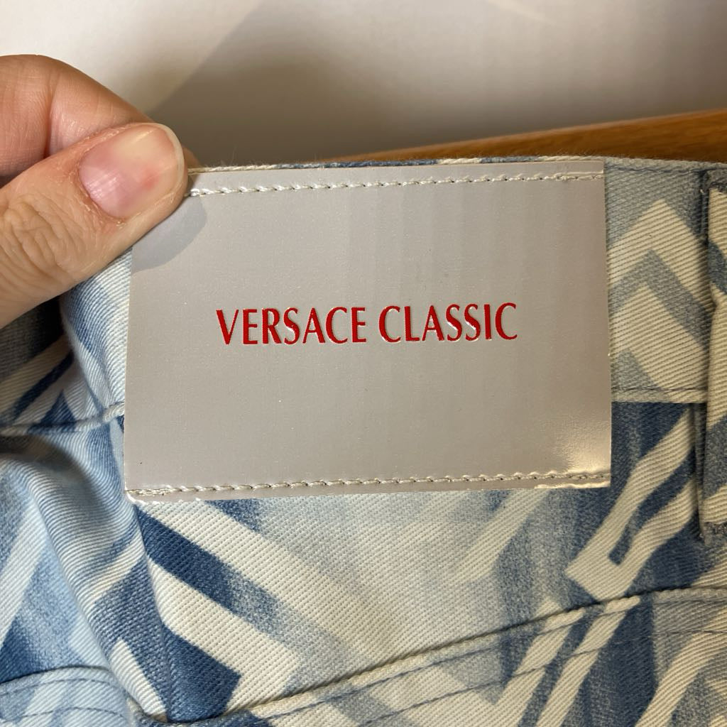 Hand holding a Versace Classic label on a garment with a neutral background