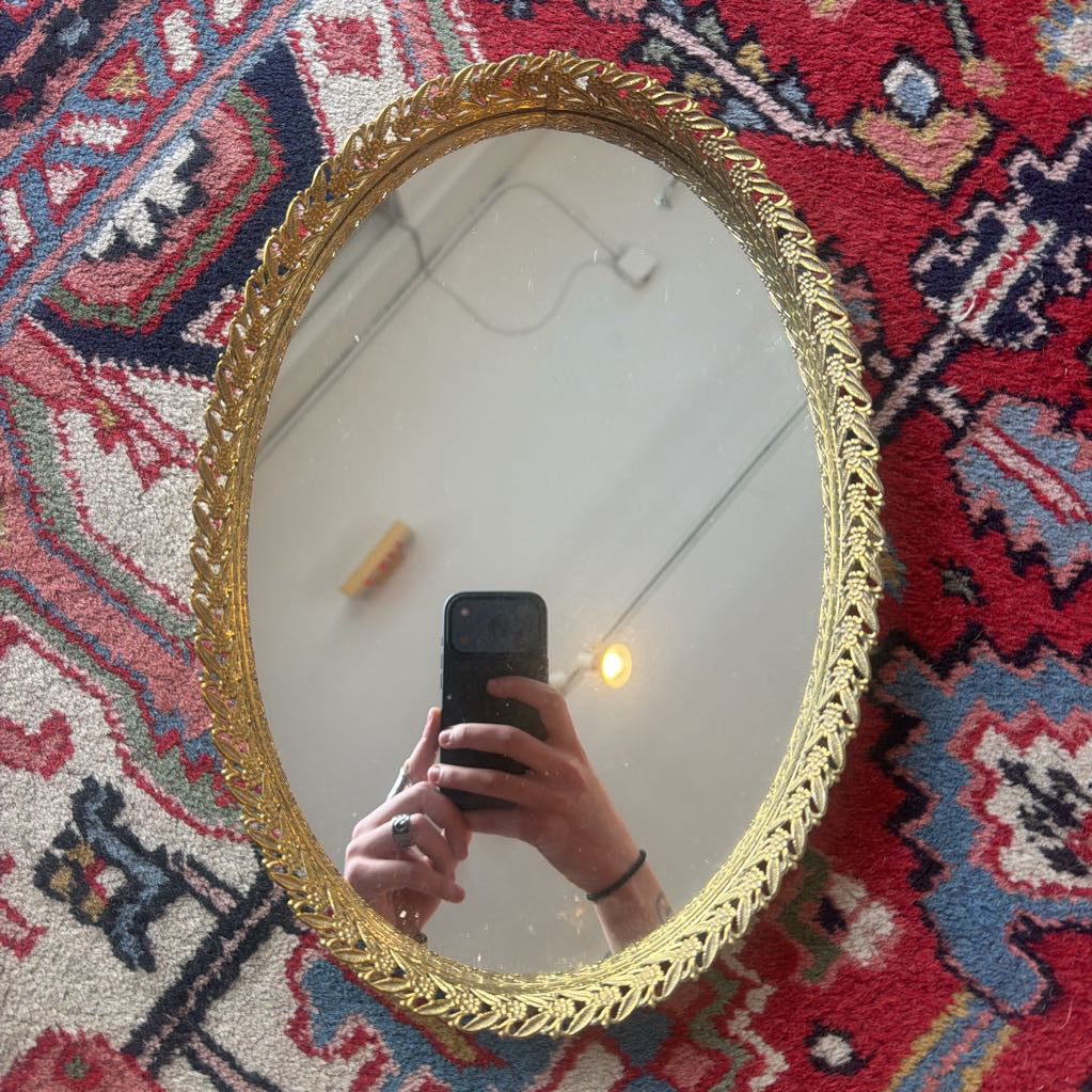 Gold-framed mirror on a colorful patterned rug with a hand holding a phone.