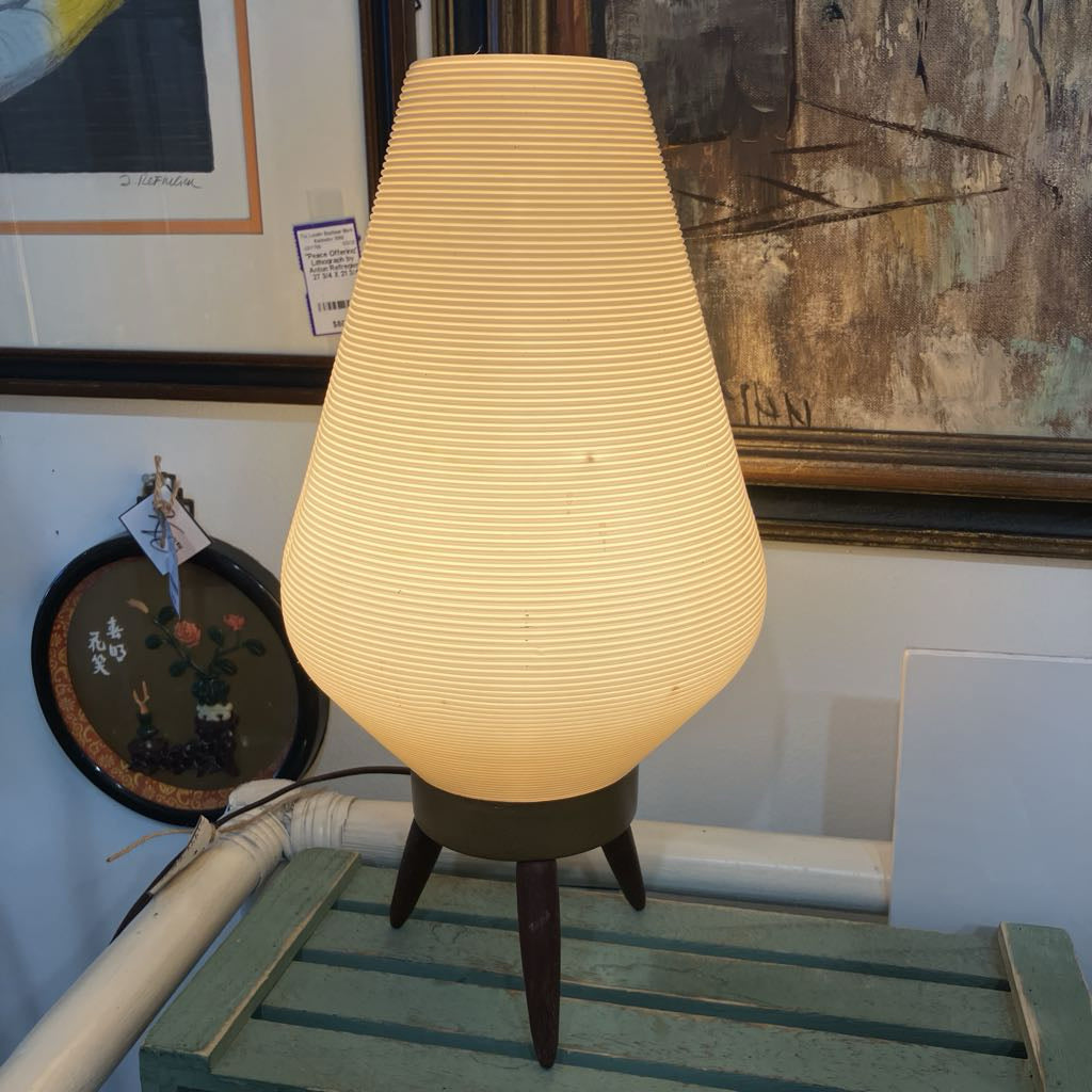 Vintage-style lamp with a ribbed shade on a wooden surface, surrounded by framed artwork.