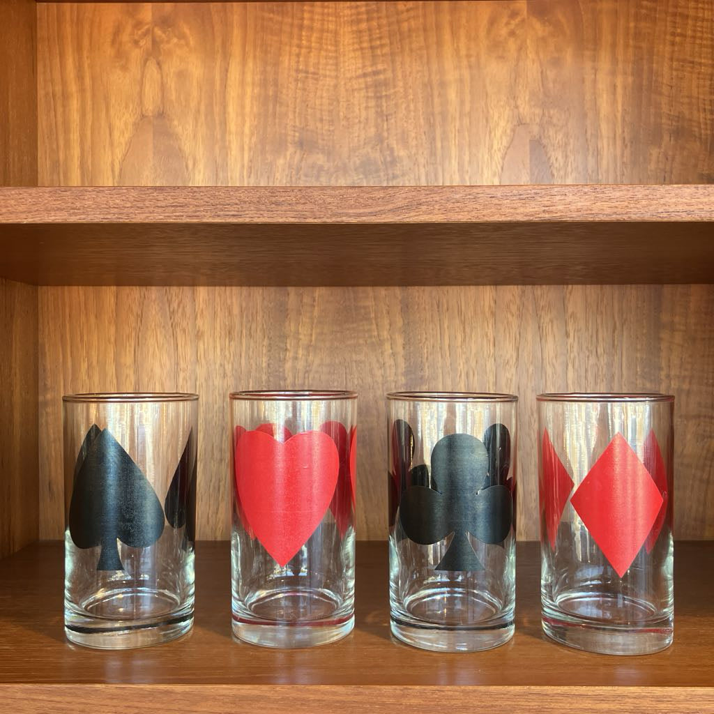 Four glass tumblers with playing card suits on a wooden shelf.