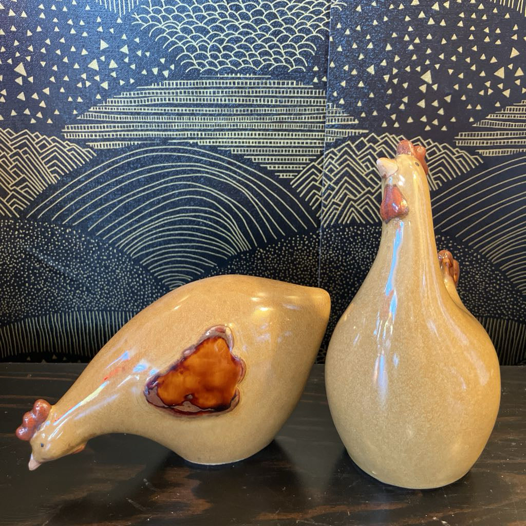 Two ceramic chicken figures on a dark surface with a patterned blue and white background.