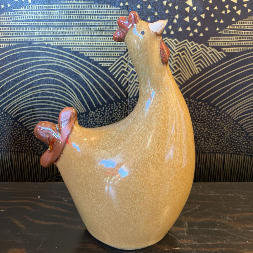 Ceramic chicken figurine on a wooden surface with a patterned wall in the background