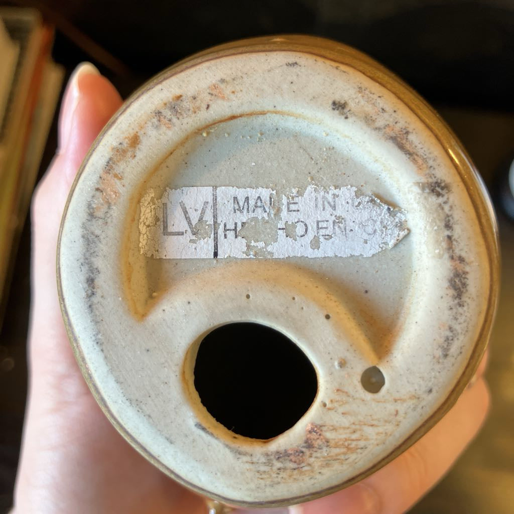 Close-up of a ceramic object with a label held by a hand.