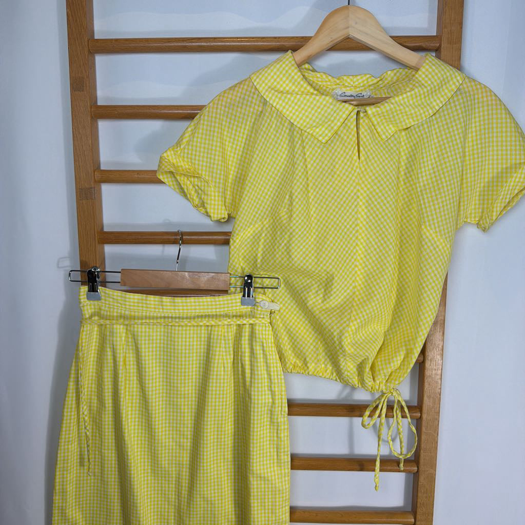 Yellow checkered outfit with top and a skirt on a wooden rack against a white background