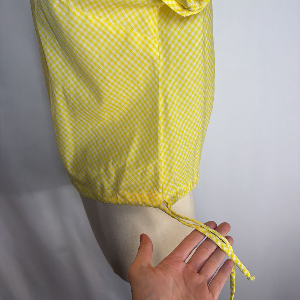 Yellow checkered shirt with a hand pulling on the drawstring against a light gray background