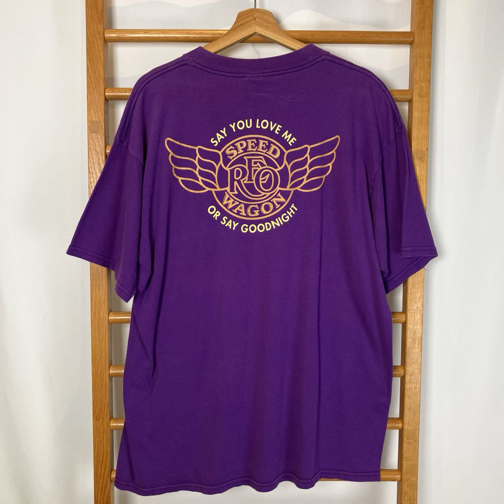 Purple t-shirt with gold logo and text on a wooden hanger against a white wall