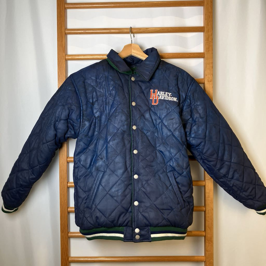 Blue quilted jacket with Harley Davidson logo on a wooden rack against a white wall.