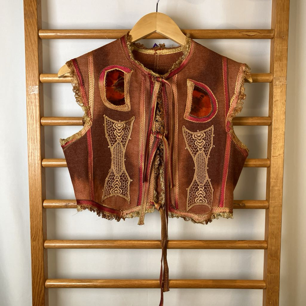 Decorative vest with intricate patterns hanging on a wooden rack.