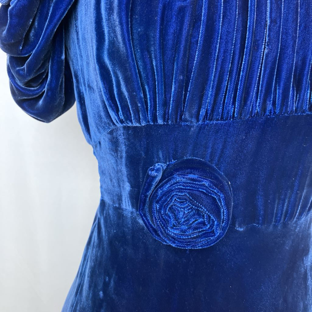 Close-up of a blue velvet dress with a decorative button on a white background