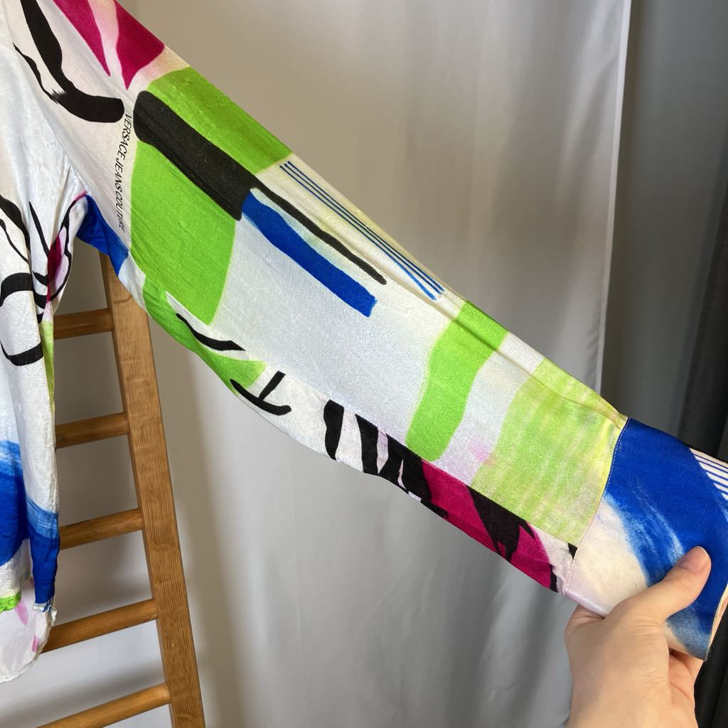 Colorful abstract patterned fabric held by a person on a ladder against a plain wall.