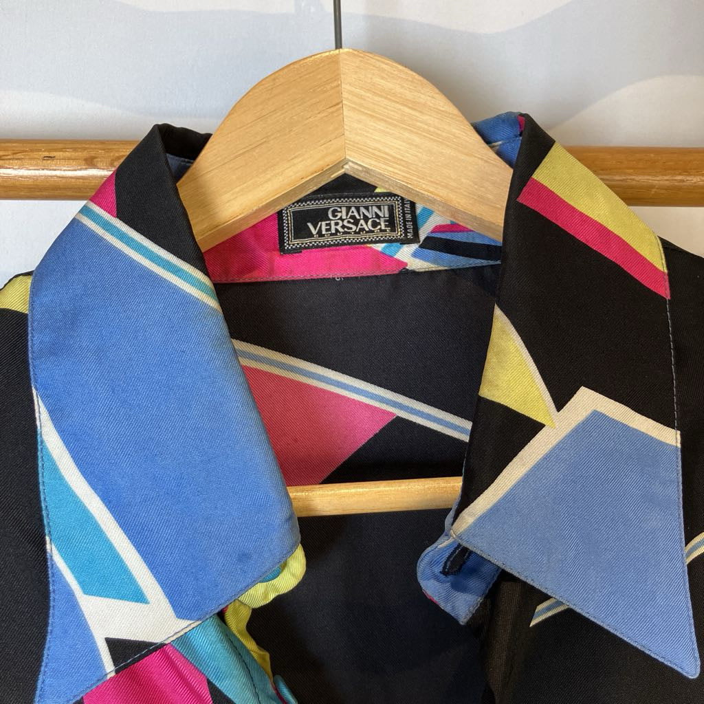 Colorful geometric-patterned jacket with a Gianni Versace hanger on a wooden rack.