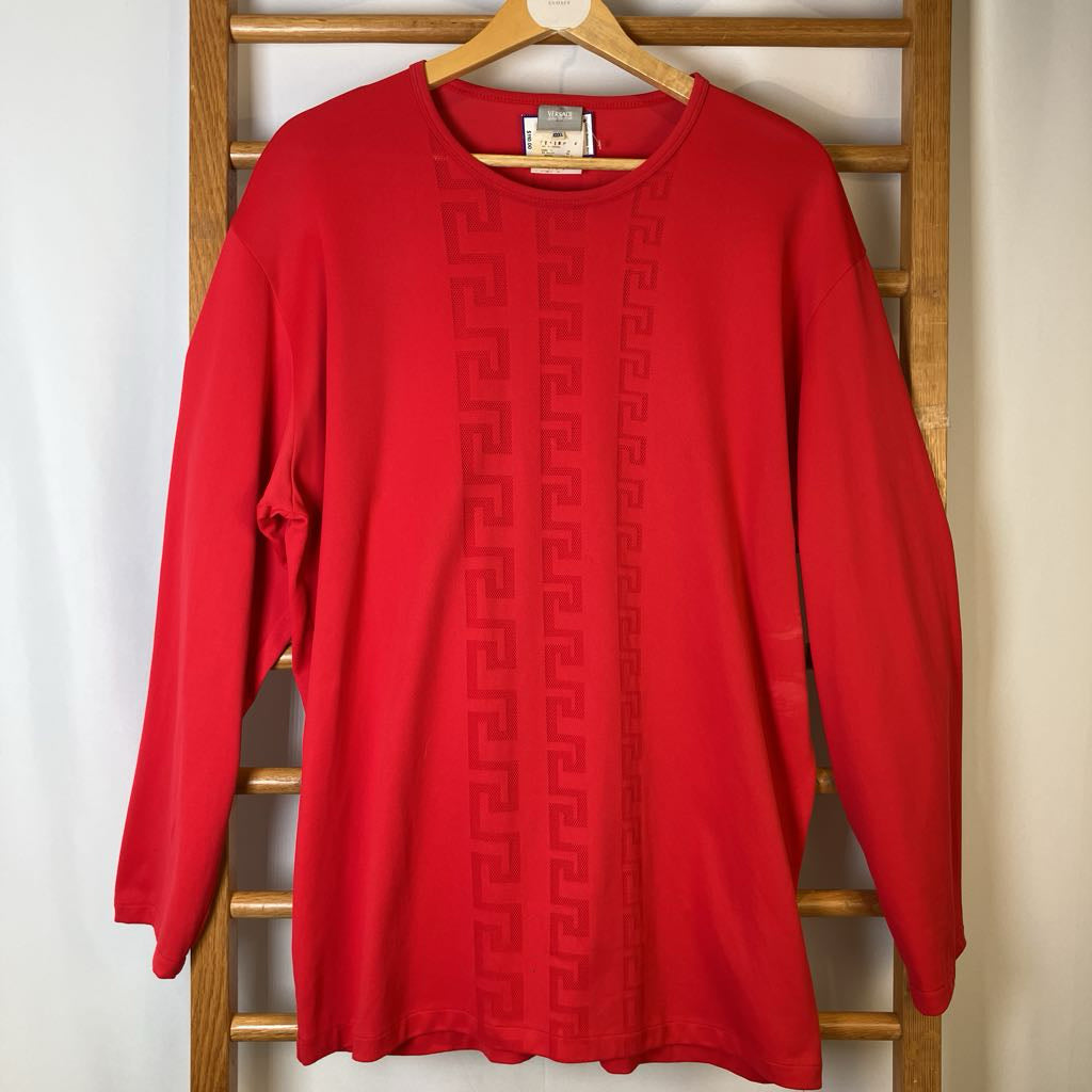 Red sweater with a pattern on a wooden hanger against a white wall
