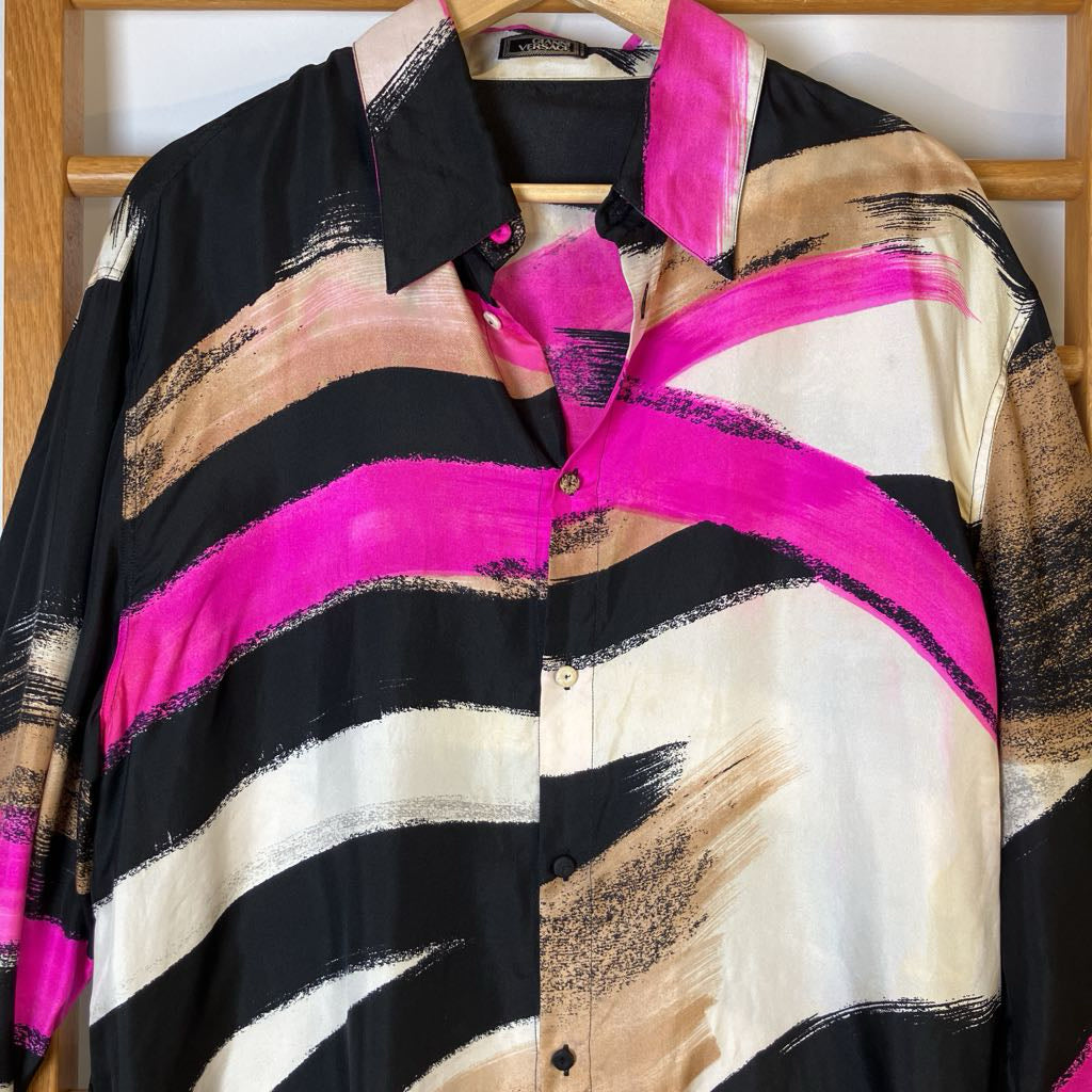 Colorful striped shirt with black, pink, beige, and white pattern on a wooden hanger.