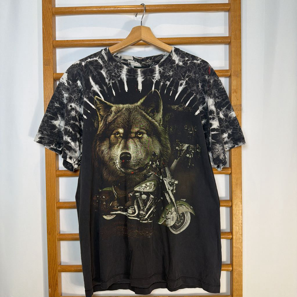 Tie-dye t-shirt with a wolf on a motorcycle graphic, hanging on a wooden rack.