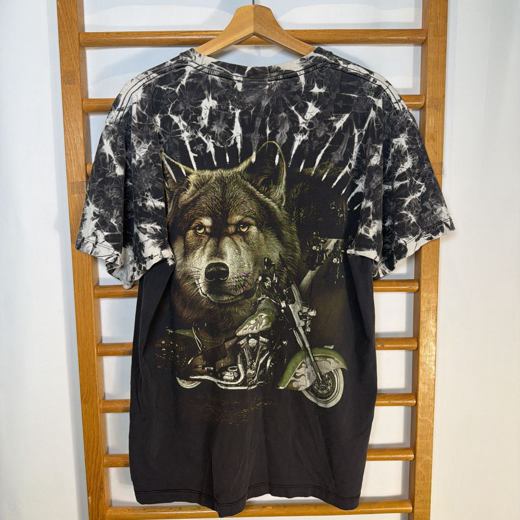 Tie-dye t-shirt with a wolf on a motorcycle graphic, hanging on a wooden rack.