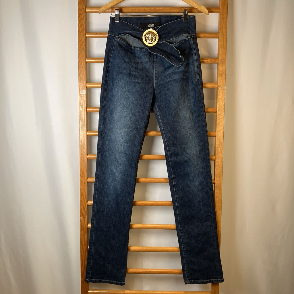 Blue jeans with a gold belt buckle on a wooden rack against a beige background
