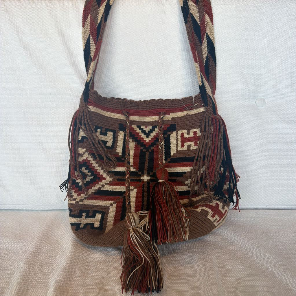 Handcrafted bag with intricate patterns and tassels on a white background